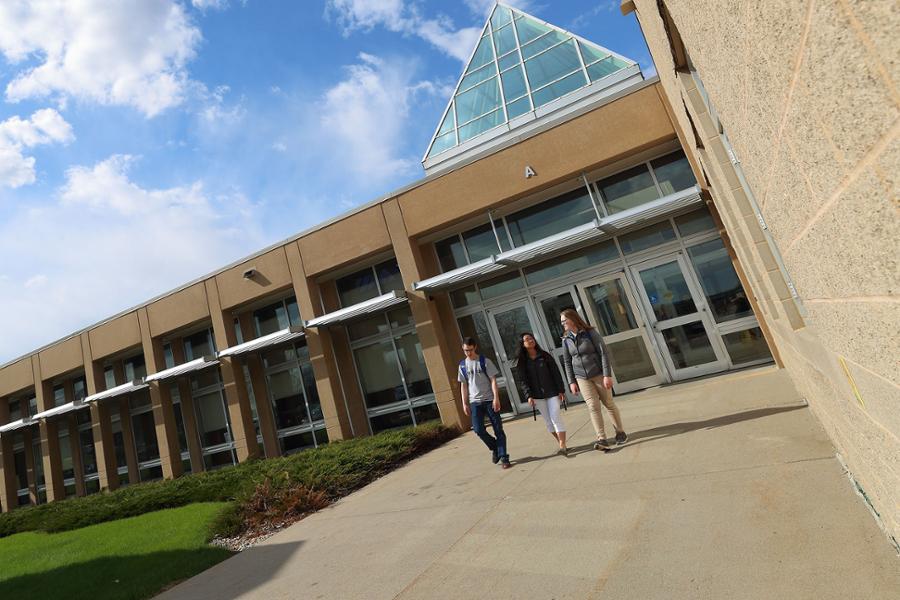 Three students walking out of health building on sunny day