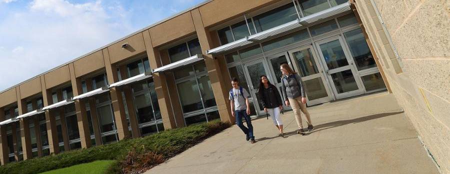 Three students walking on sidewalk in sunshine by health building