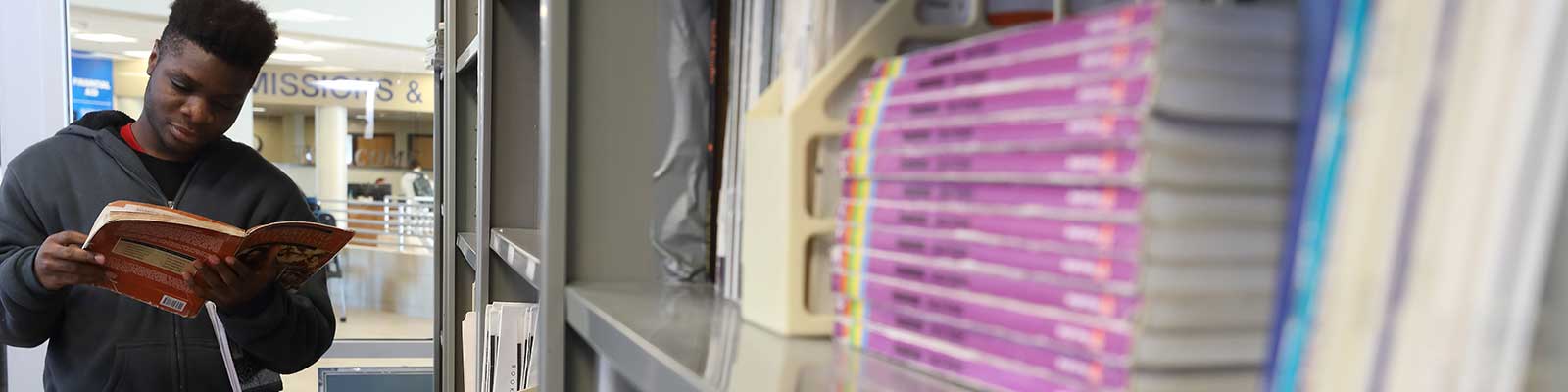 Student reads a book near a bookshelf