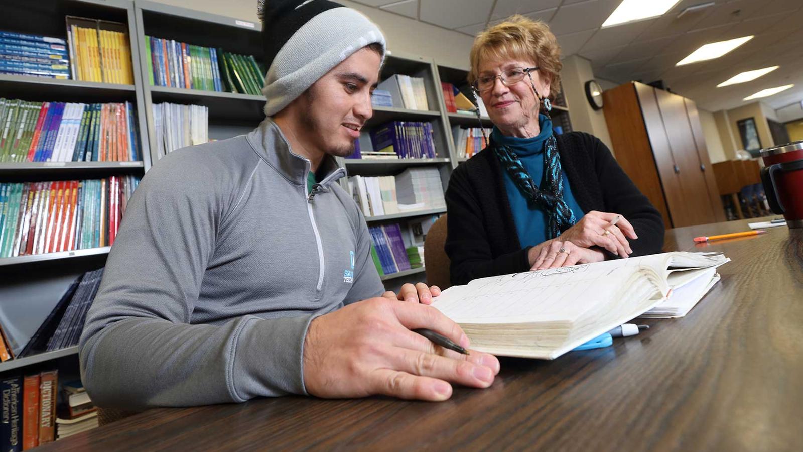 Student with teacher and open book at large table