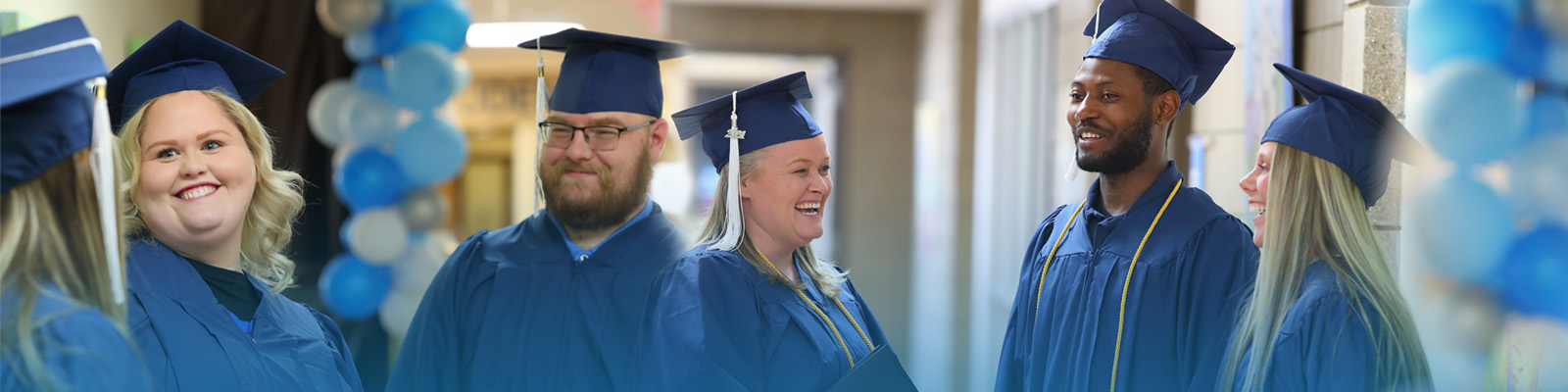 graduates smiling in hallway with blue toned balloons