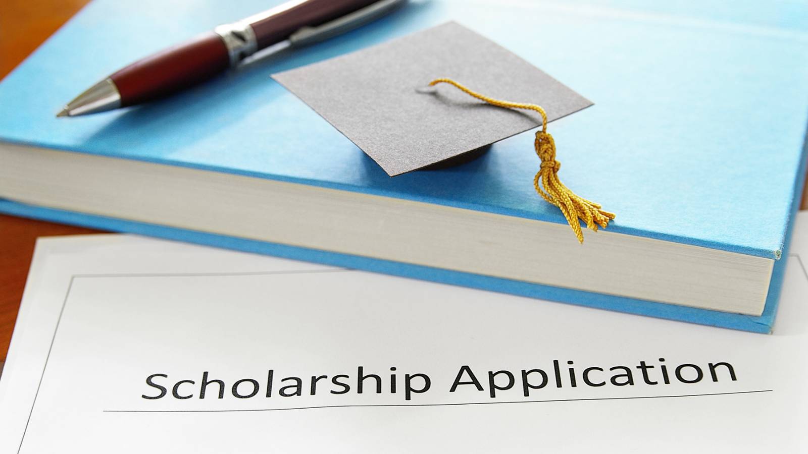Scholarships at Southeast Tech Paper scholarship application, with a book and miniture graduation cap on top