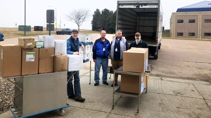 Four men standing with boxes of PPE and open truck