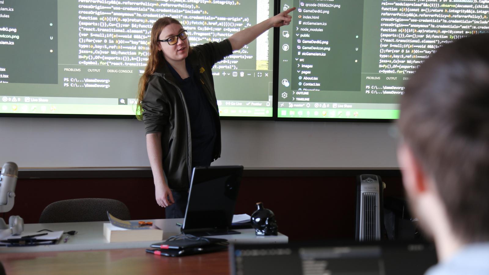 Computer programming instructor in front of screens of code