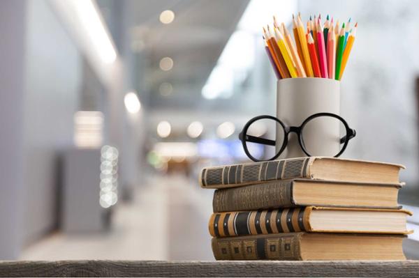 books, glasses and colored pencils stacked on a desk