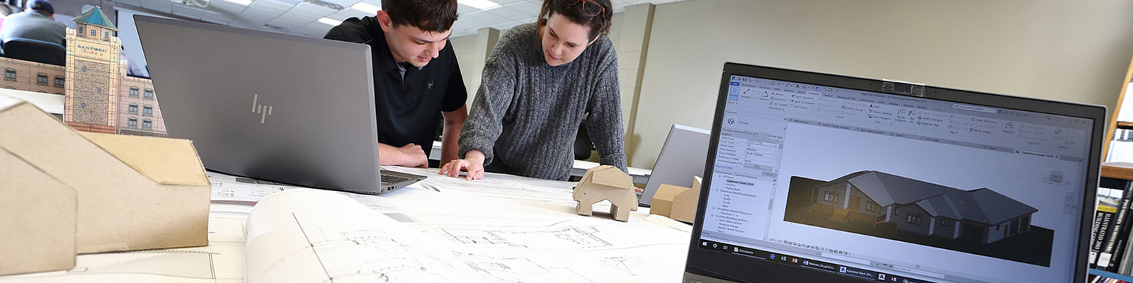 Students reviewing blueprints on table with design software and models