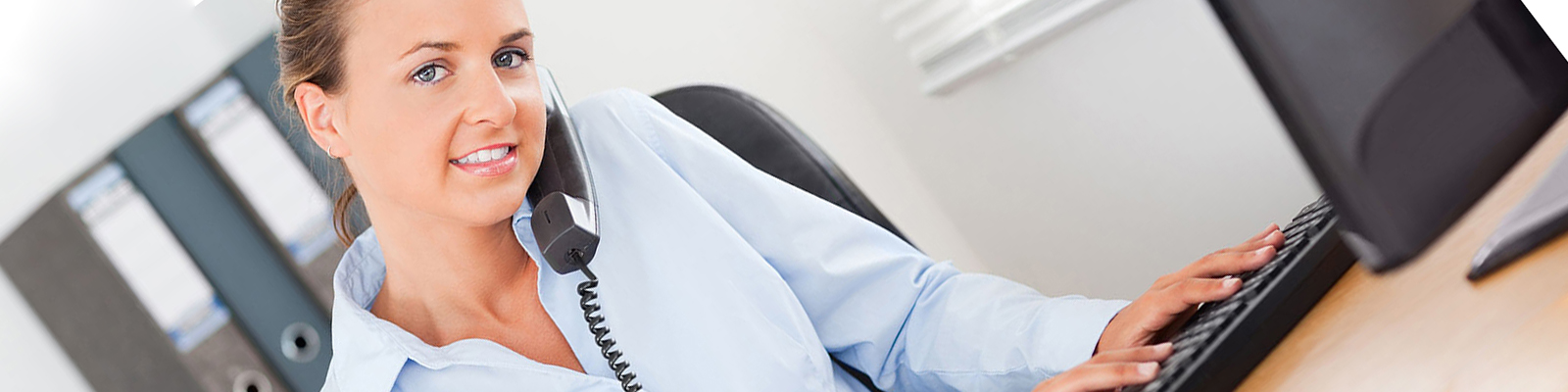 Young woman typing while on office phone