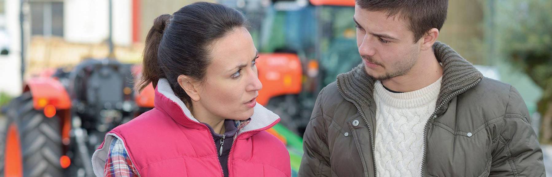 Man and woman in front of tractor, viewing information on tablet