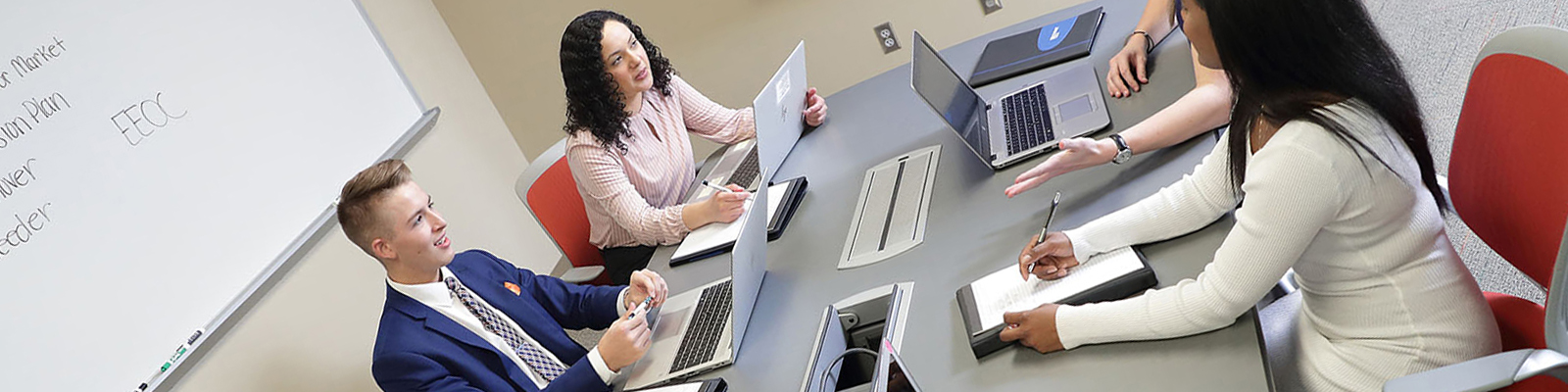 Students at conference room table with laptops, white board, and large display monitor