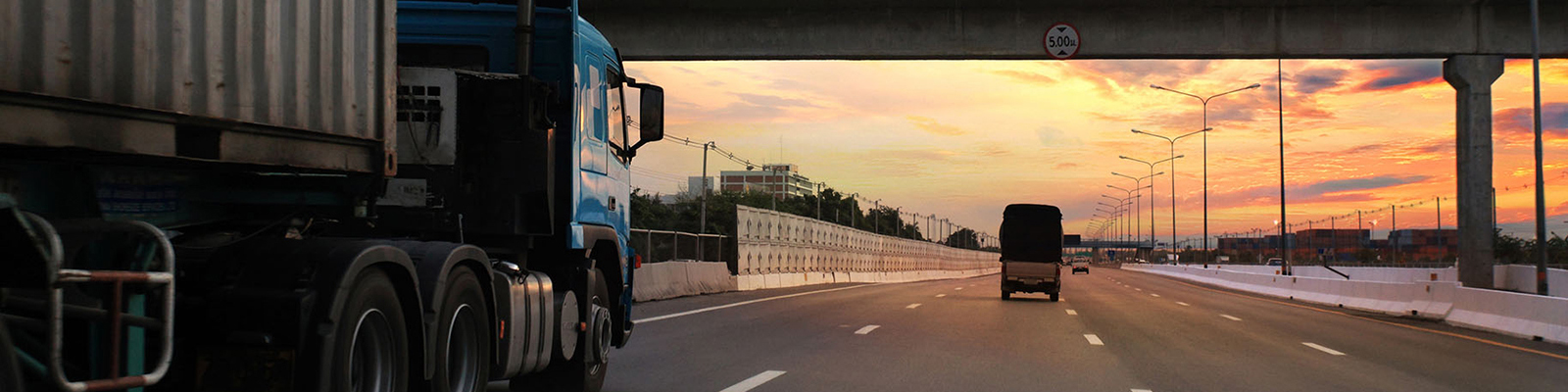 Semi truck going under an interstate bridge at sunset