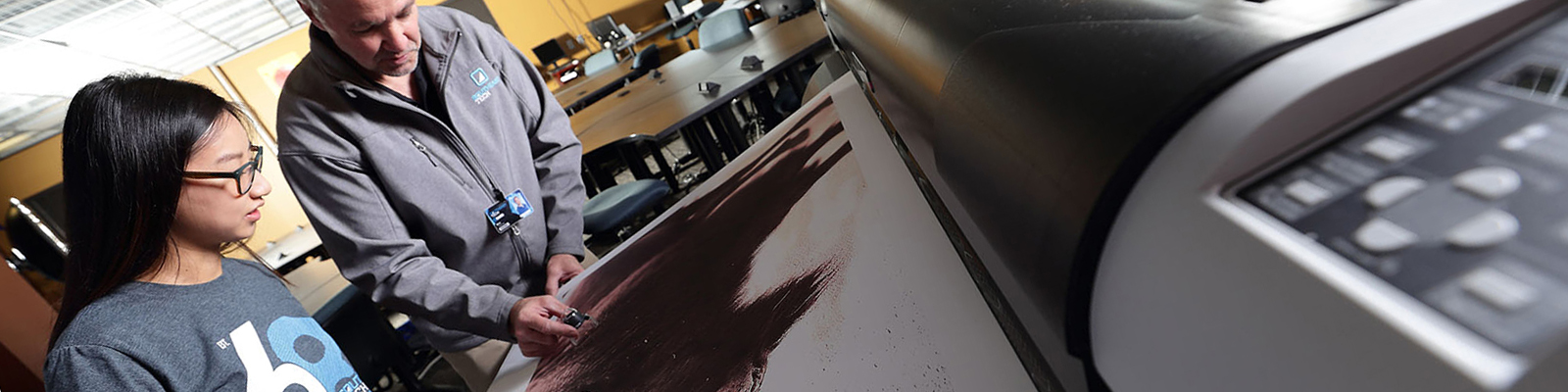 Student and instructor reviewing print from large-scale printer