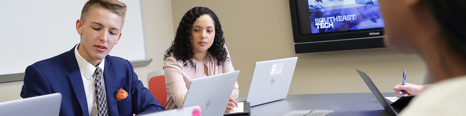 Students in business apparel working at a conference room table. Southeast Tech image displayed on screen.