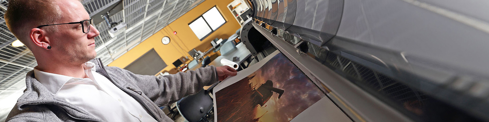 Male student examining print on large scale printer