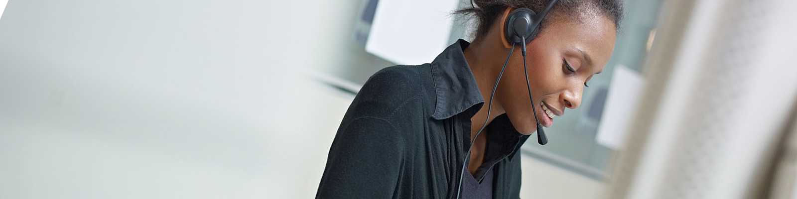 Woman in call center setting wearing a headset and working in front of a computer.