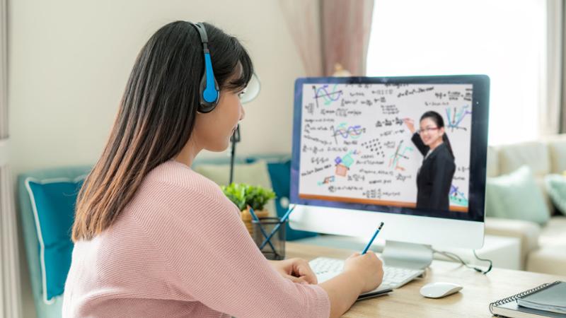 Female student working at home desk with instructor on desktop computer screen