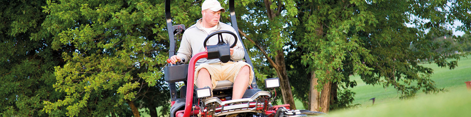 Man on large riding lawnmower, trimming grass on a golf course.