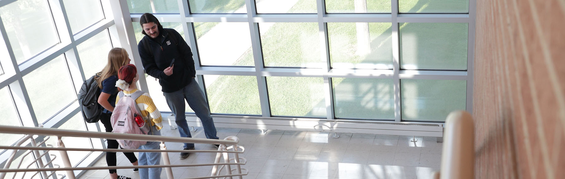 students in sunny stairwell with green grass and green trees outside.