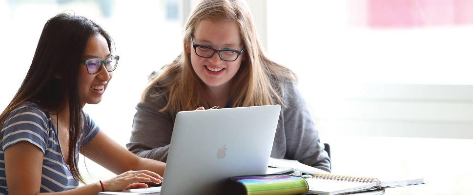 Two students studying with open laptop and stack of books