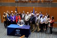 Governor signing a bill with a crowd around him.